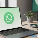 Laptop na mesa com a tela exibindo o logo do WhatsApp para explicar como baixar e instalar WhatsApp, logo ao lado de um celular e mouse, com ambiente de escritório ao fundo.